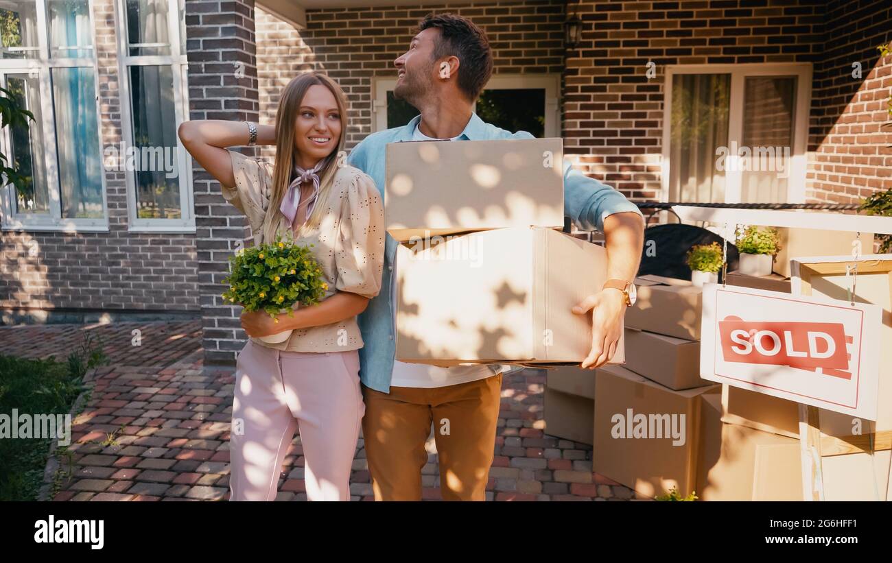 happy couple with boxes and plant standing near new house Stock Photo ...