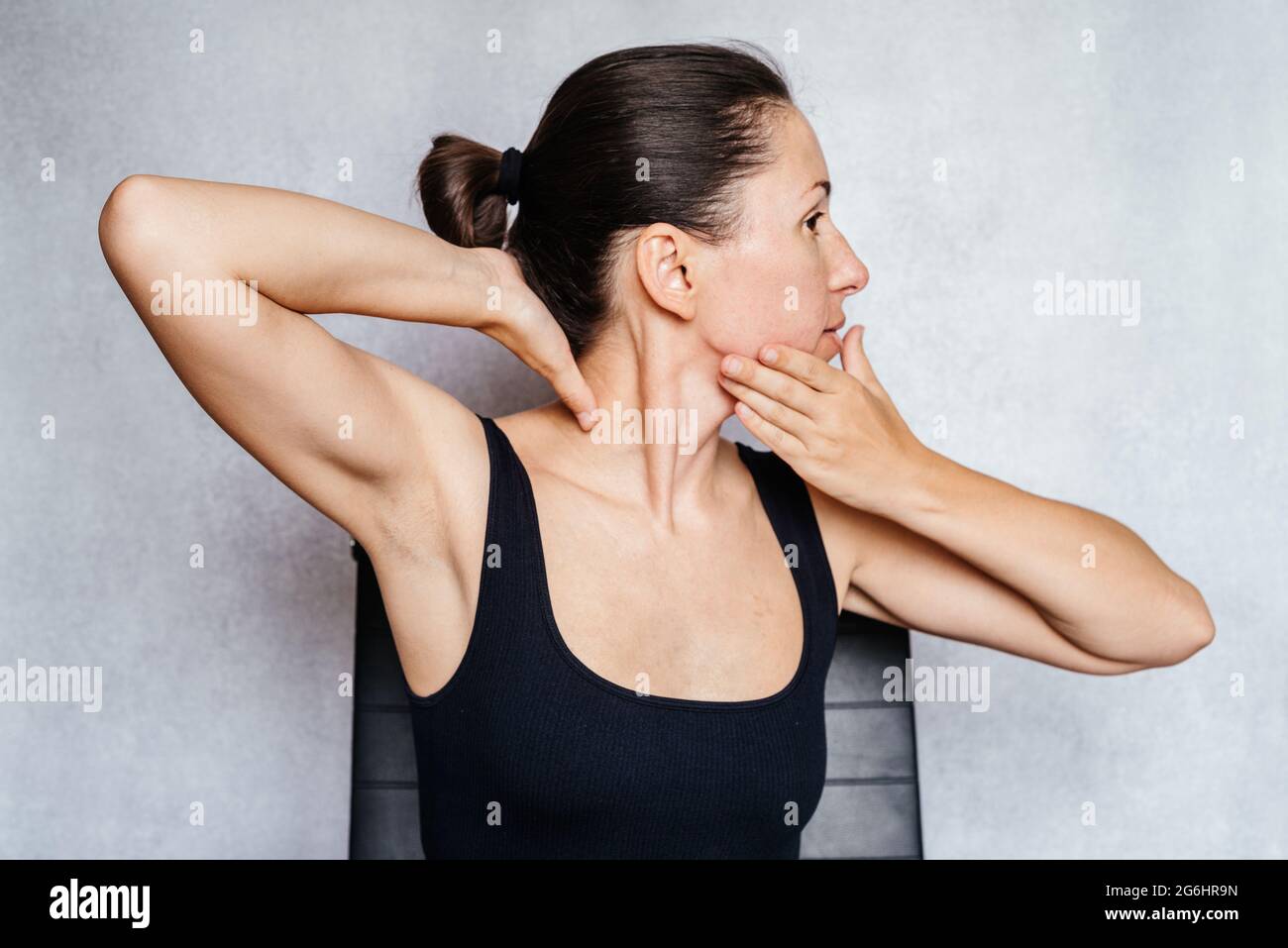 A woman gently rotates her head with both hands while doing the