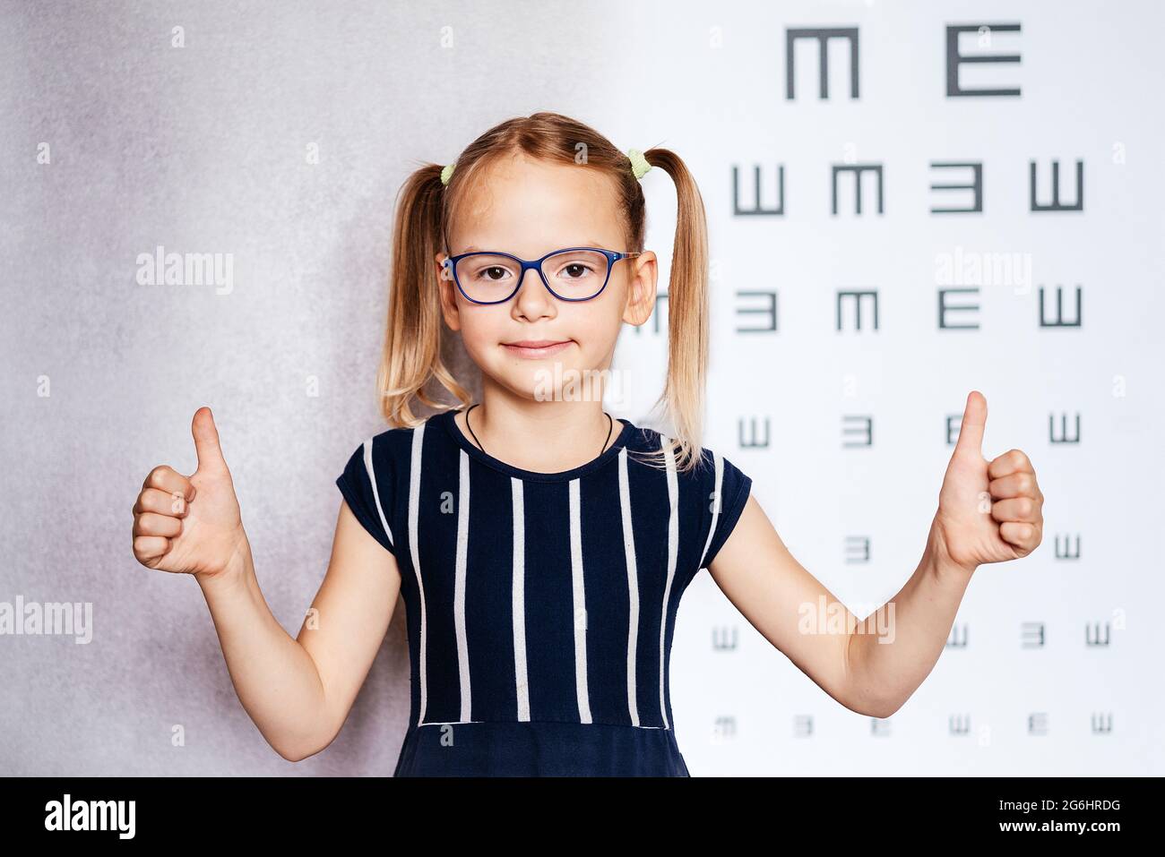 Little girl wearing eyeglasses with her thumbs up taking eyesight test