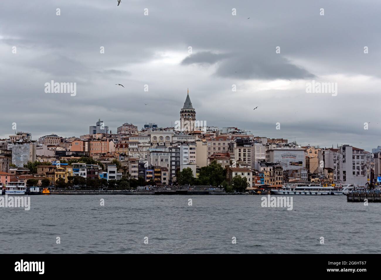 Galata Tower within residential buildings in old town. Karakoy coastal view from Bosporus. Sea and Golden Horn on a cloudy day. Stock Photo