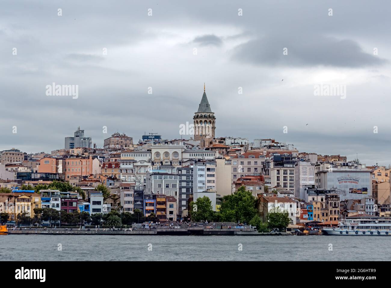 Galata Tower within residential buildings in old town. Karakoy coastal view from Bosporus. Sea and Golden Horn on a cloudy day. Stock Photo
