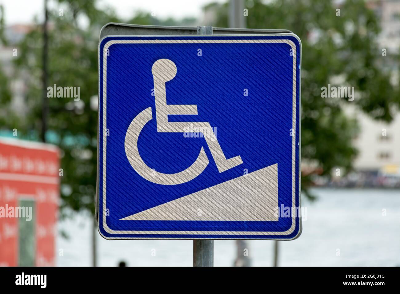 Disabled Ramp Access Sign in the city. Green foliage in the background. Stock Photo