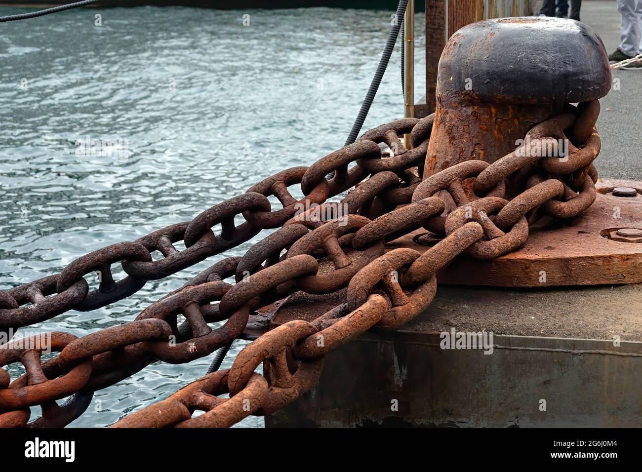 Stud link type rusty ship anchor chain and one headed mooring bitt on a ferry port. Stock Photo