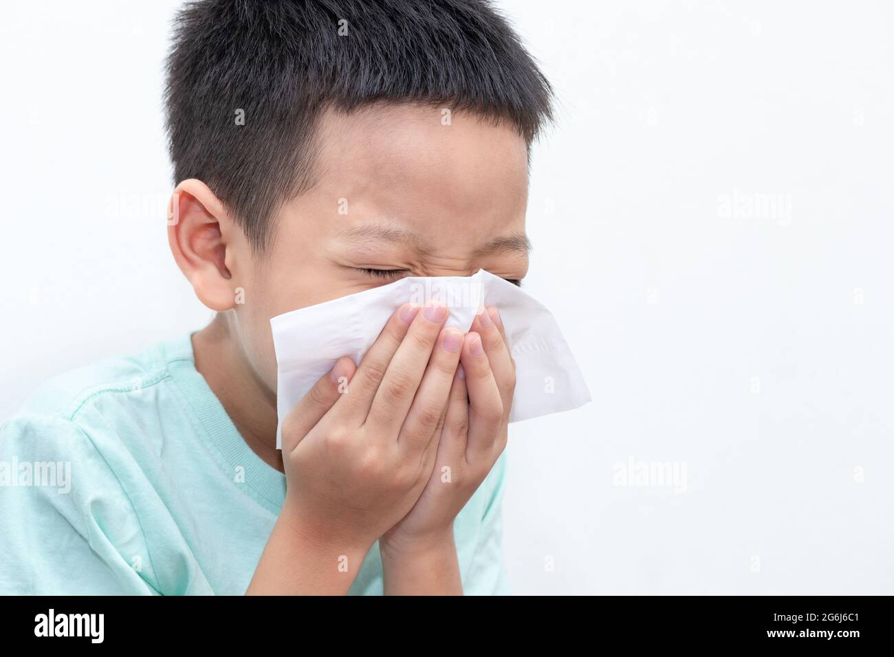 Asian little boy blowing his nose or cleaning nose with tissue. The little boy was sick and was sneezing isolated white background. Stock Photo