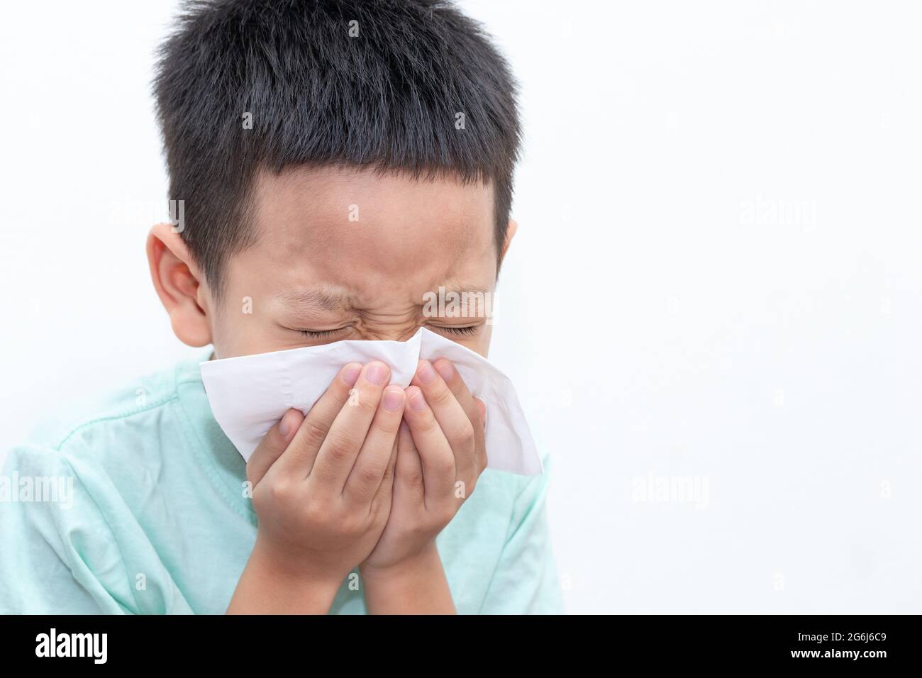 Asian little boy blowing his nose or cleaning nose with tissue. The little boy was sick and was sneezing isolated white background. Stock Photo