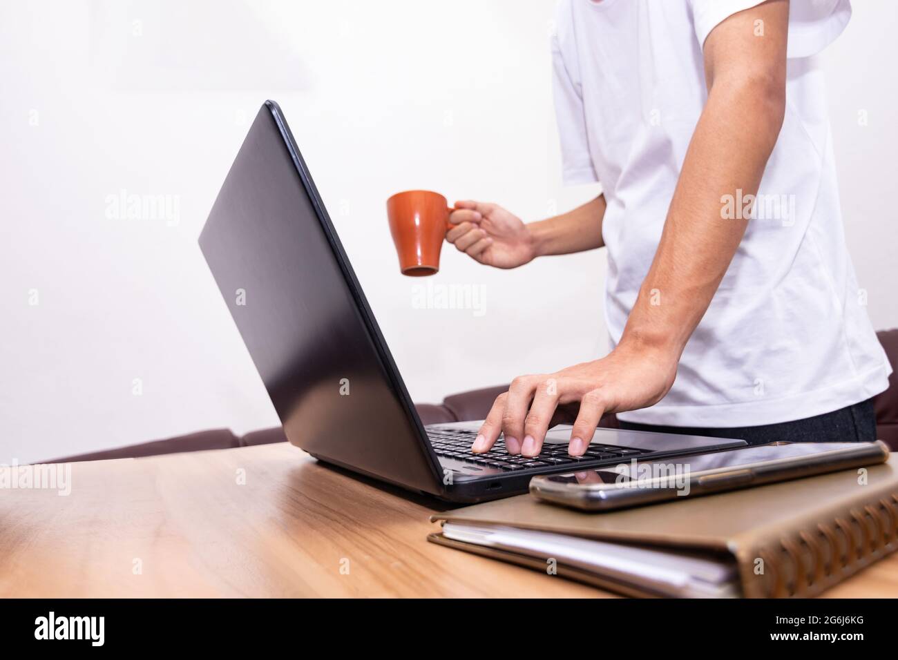 The businessman is standing holding a coffee cup and working on a laptop at his home. technology, people, and lifestyle concept. Stock Photo