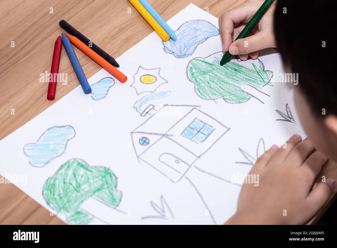 A little boy drawing a house with crayons is a beautiful imagination painting. A little child is engaged in creativity, the child does his homework. Stock Photo