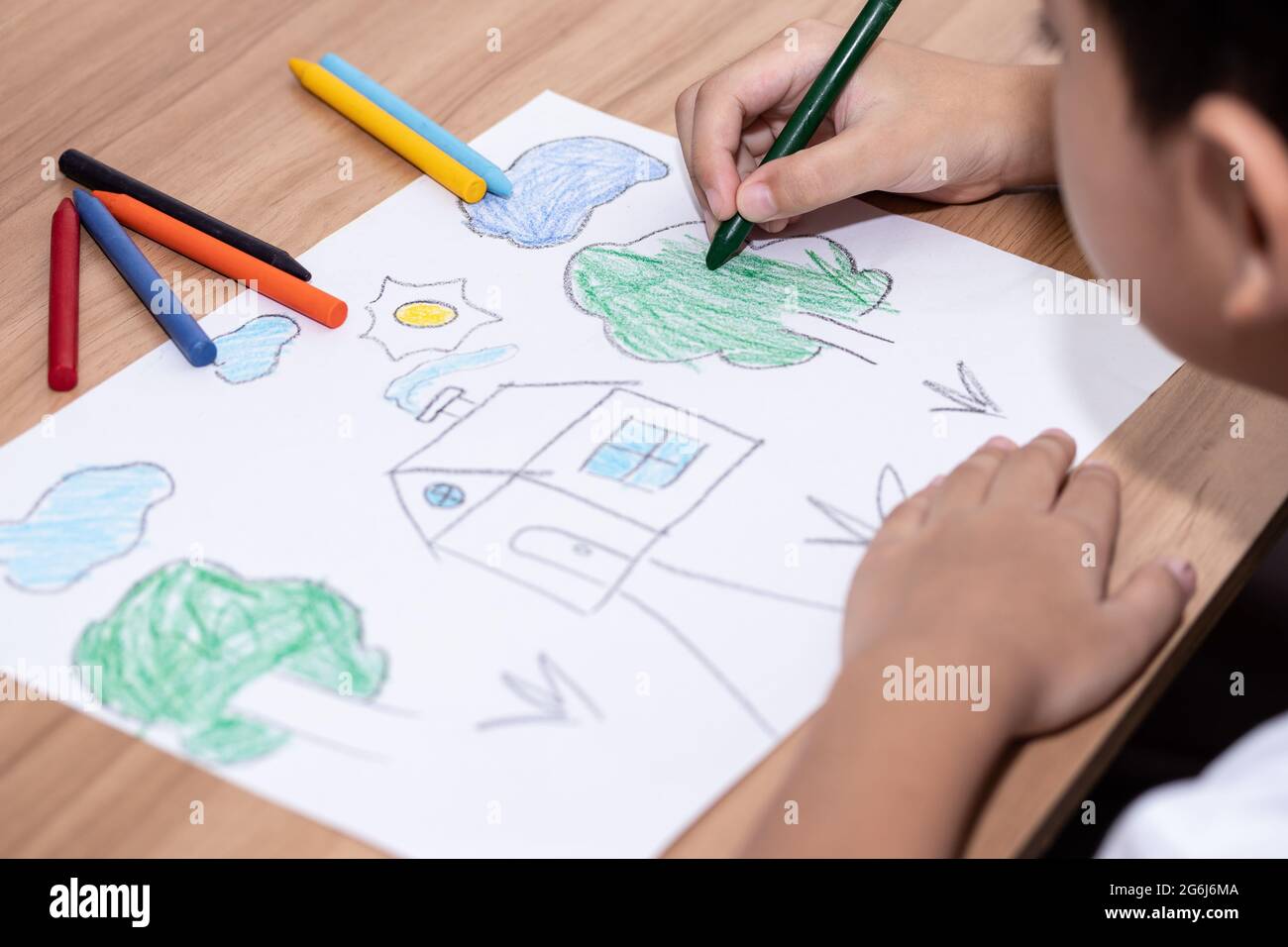 A little boy drawing a house with crayons is a beautiful imagination painting. A little child is engaged in creativity, the child does his homework. Stock Photo