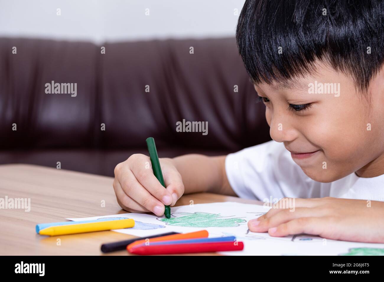 A little Asian boy is happily drawing a house with crayons is a beautiful imagination painting. A little child is engaged in creativity, the child doe Stock Photo