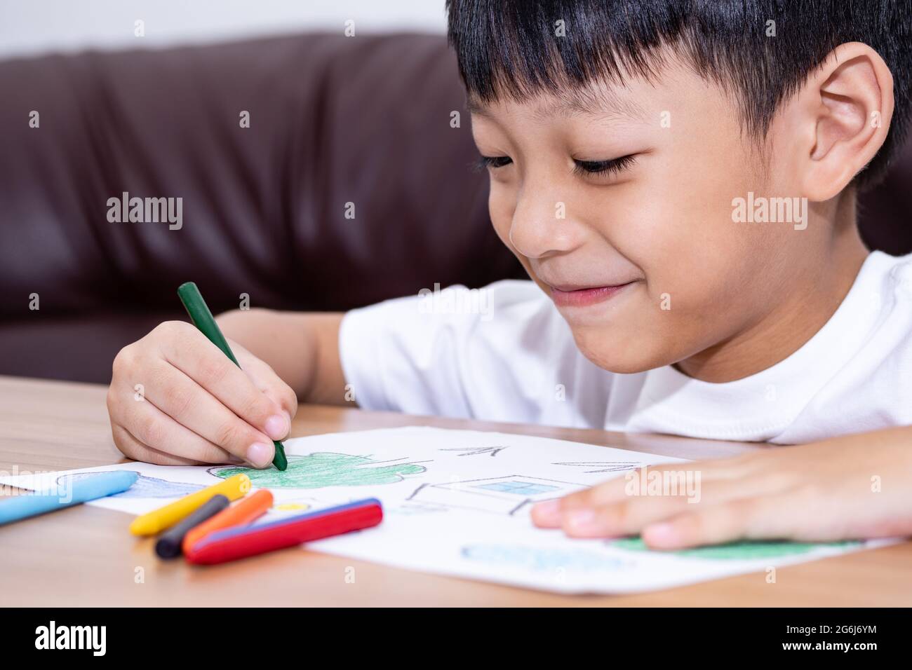 A little Asian boy is happily drawing a house with crayons is a beautiful imagination painting. A little child is engaged in creativity, the child doe Stock Photo