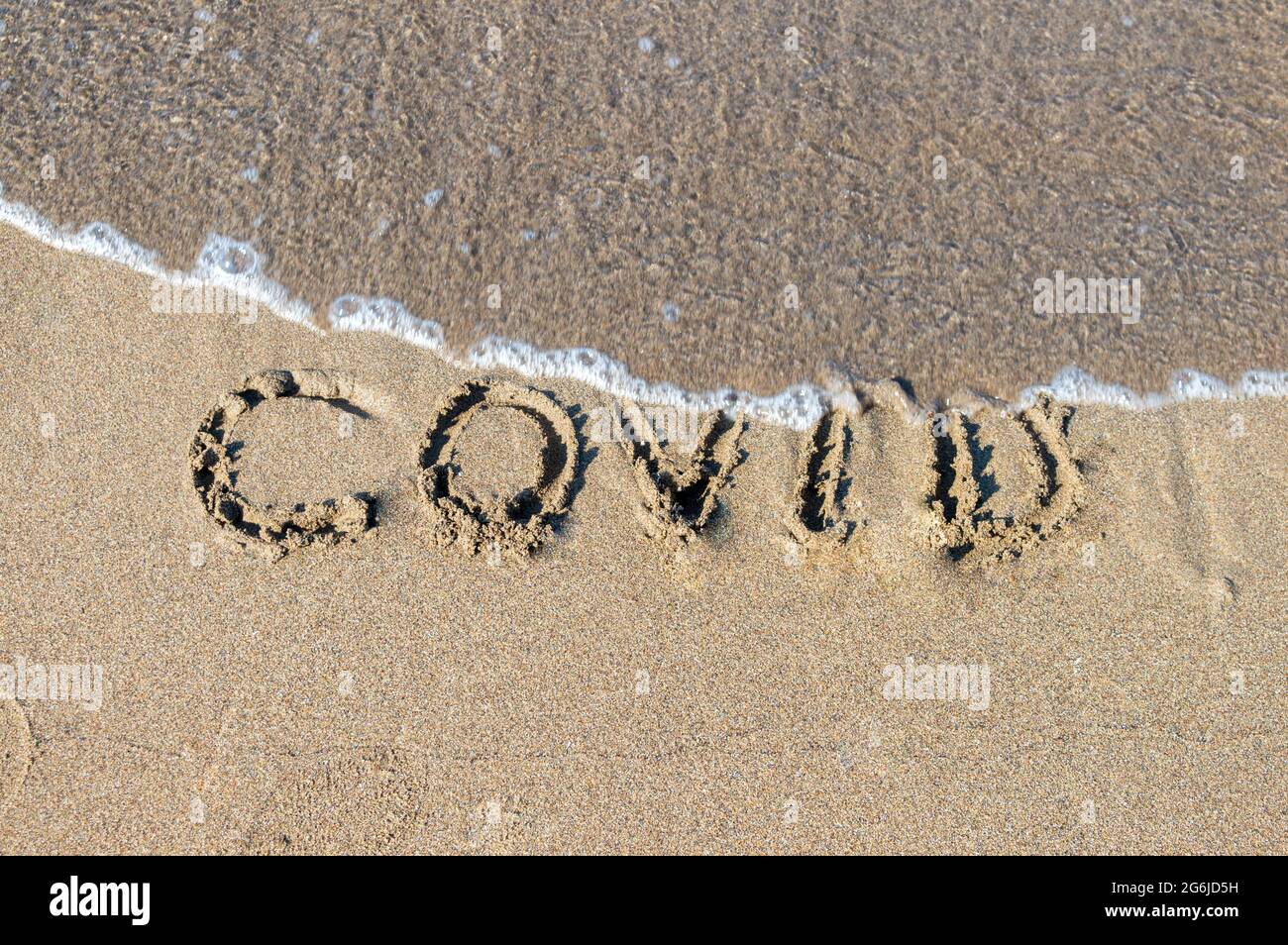 covid text on the sand on the beach. Waves from the sea erase the covid text. Removal of tourism restrictions in summer, opening of beaches.Covid free Stock Photo