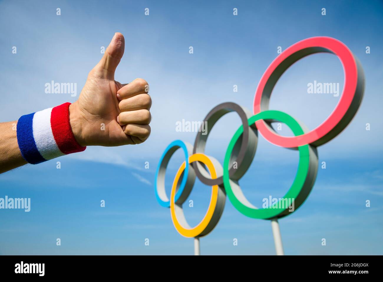 RIO DE JANEIRO - MAY 4, 2016: Athlete's hand wearing red white and blue colored wristband gives a thumbs-up gesture in front of Olympic Rings standing Stock Photo