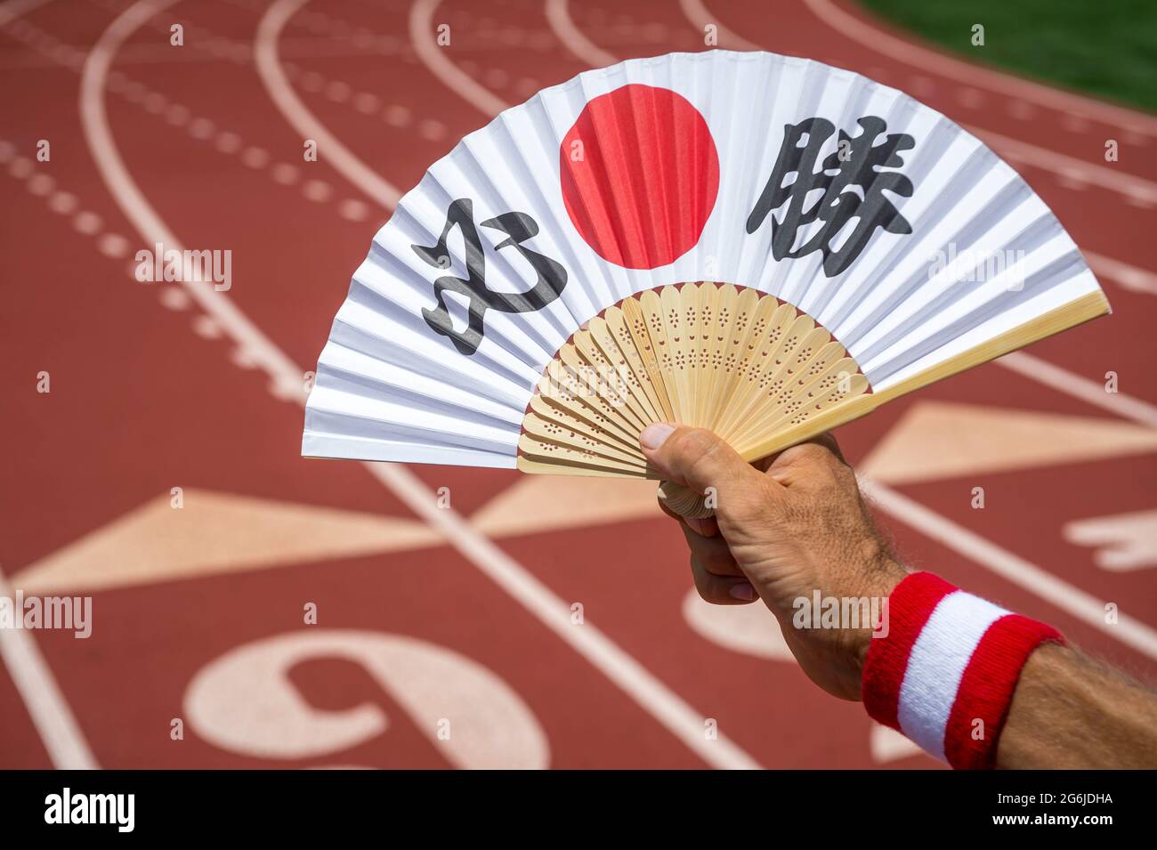 Hand of Japanese sports athlete holding a fan decorated with kanji characters spelling out hissho certain victory in English at starting line of a run Stock Photo