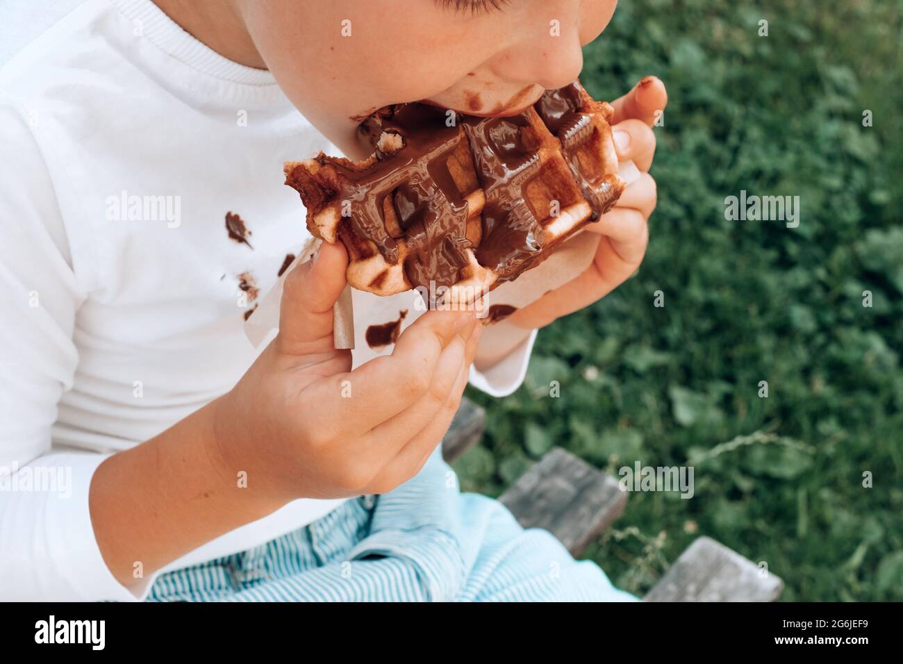 Boy eating a Belgian waffle with a chocolate topping. outdoor. daily life dirty stain for wash and clean concept. High quality photo Stock Photo