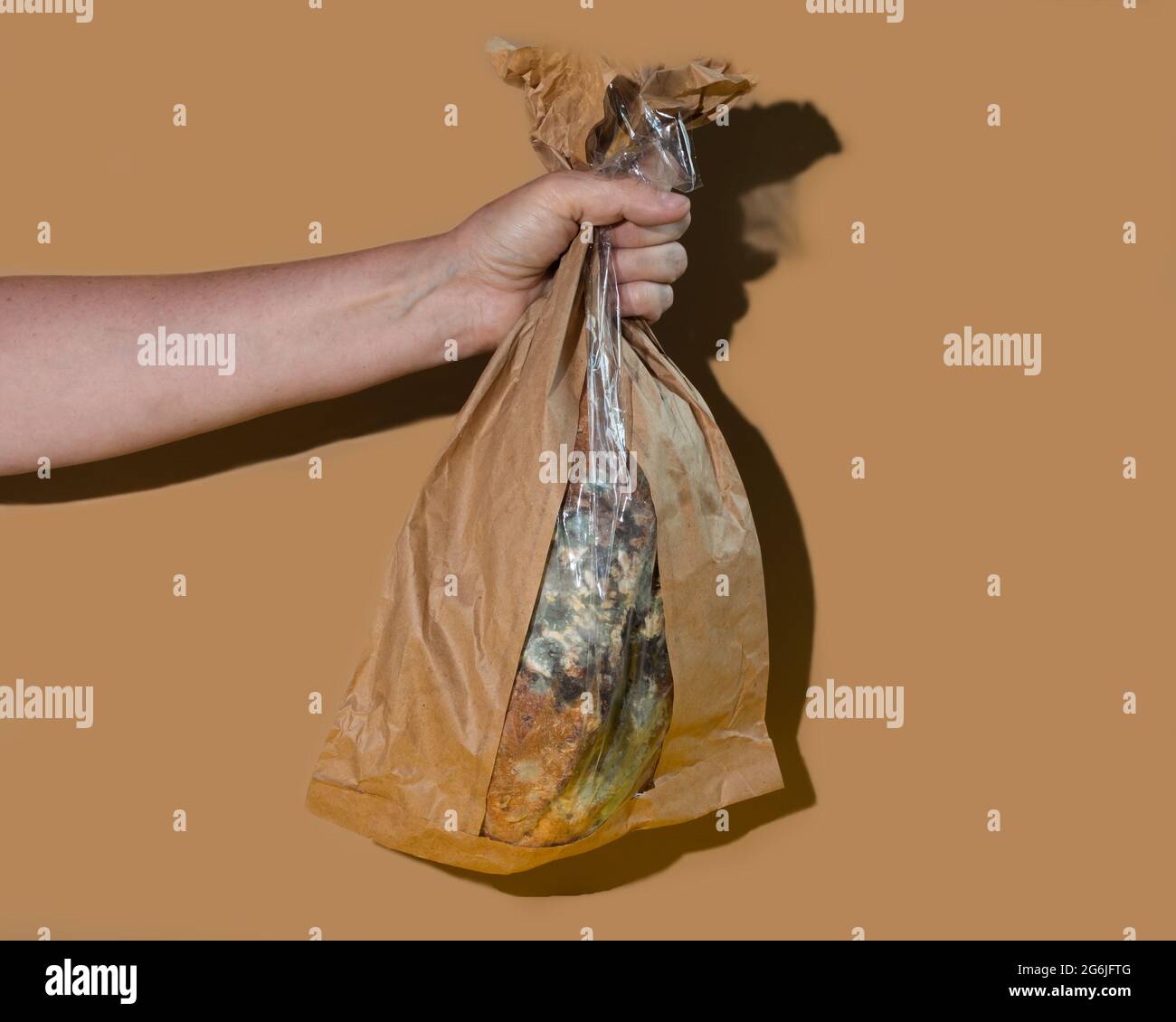 Green moldy bread on plastic wrap. Food waste concept. Minimalist style