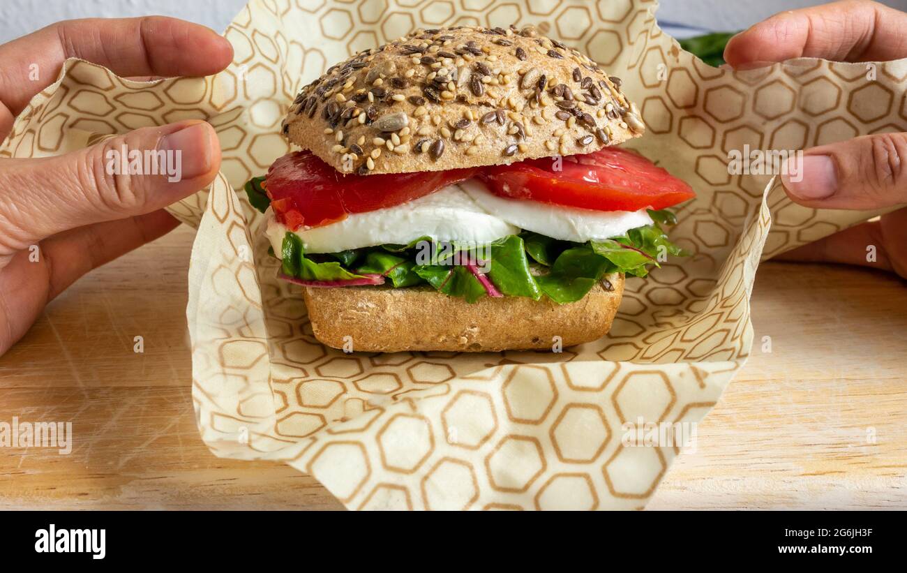 https://c8.alamy.com/comp/2G6JH3F/two-hands-packing-with-bee-wax-recyclable-wrapping-a-lunch-sandwich-with-bread-bun-mozzarella-cheese-and-lettuce-sustainable-packaging-keep-fresh-2G6JH3F.jpg