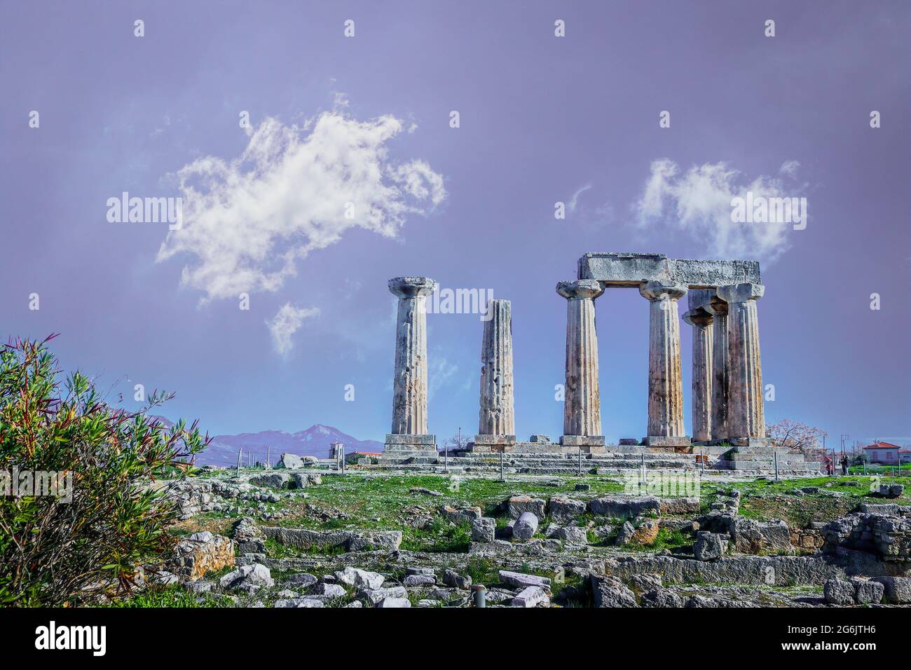 The ruins of the temple of Apollo standing tall on a hill in Corinth Greece above rubble with purple mountains in the distance and wiisy clouds overhe Stock Photo