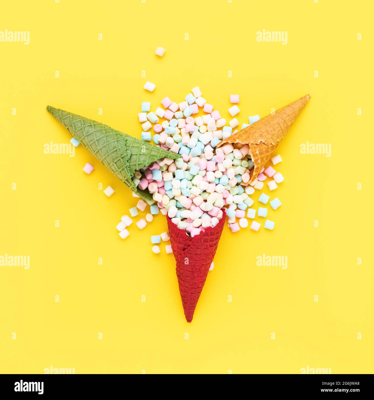 Various colors ice cream cones with marshmallows candies on a bright yellow background. Summer concept, top view Stock Photo