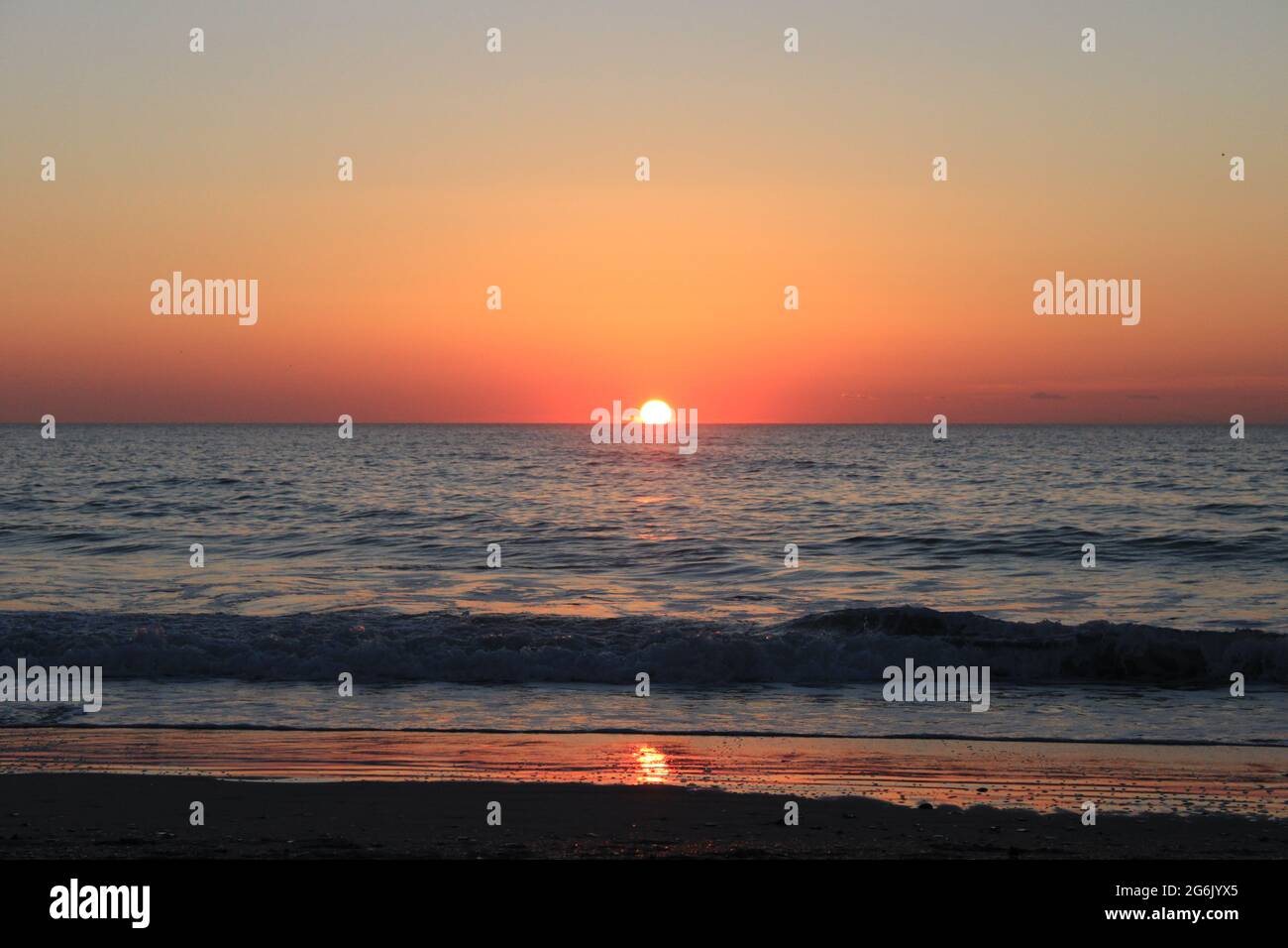 Sunrise at the beach with calm, small waves breaking slight reflection in the wet sand Stock Photo