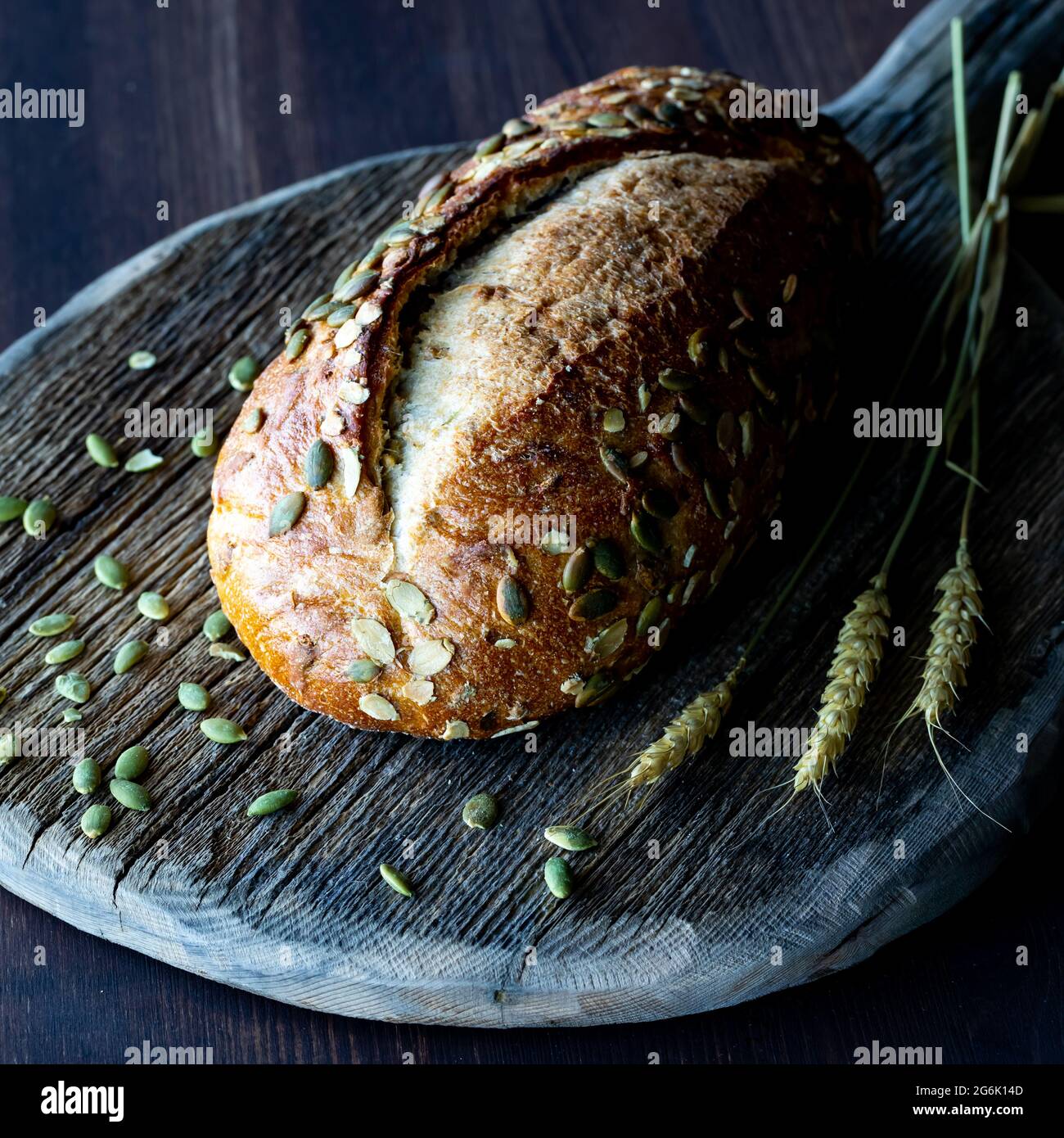 Close up view of a loaf of pumpkin seed bread on a rustic wooden board against a dark background. Stock Photo
