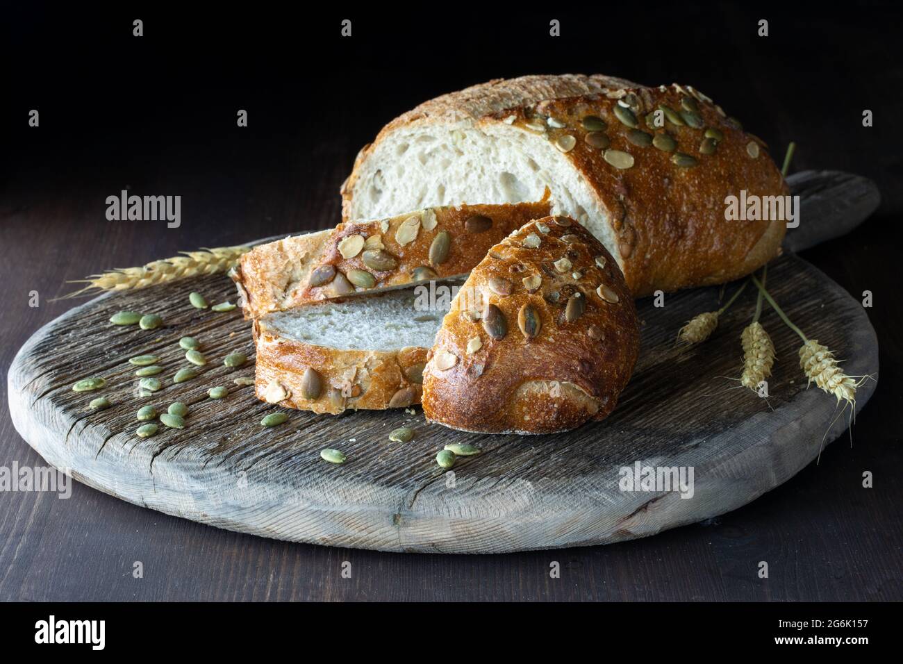 Sliced pumpkin seed bread on a rustic wooden board against a dark background. Stock Photo