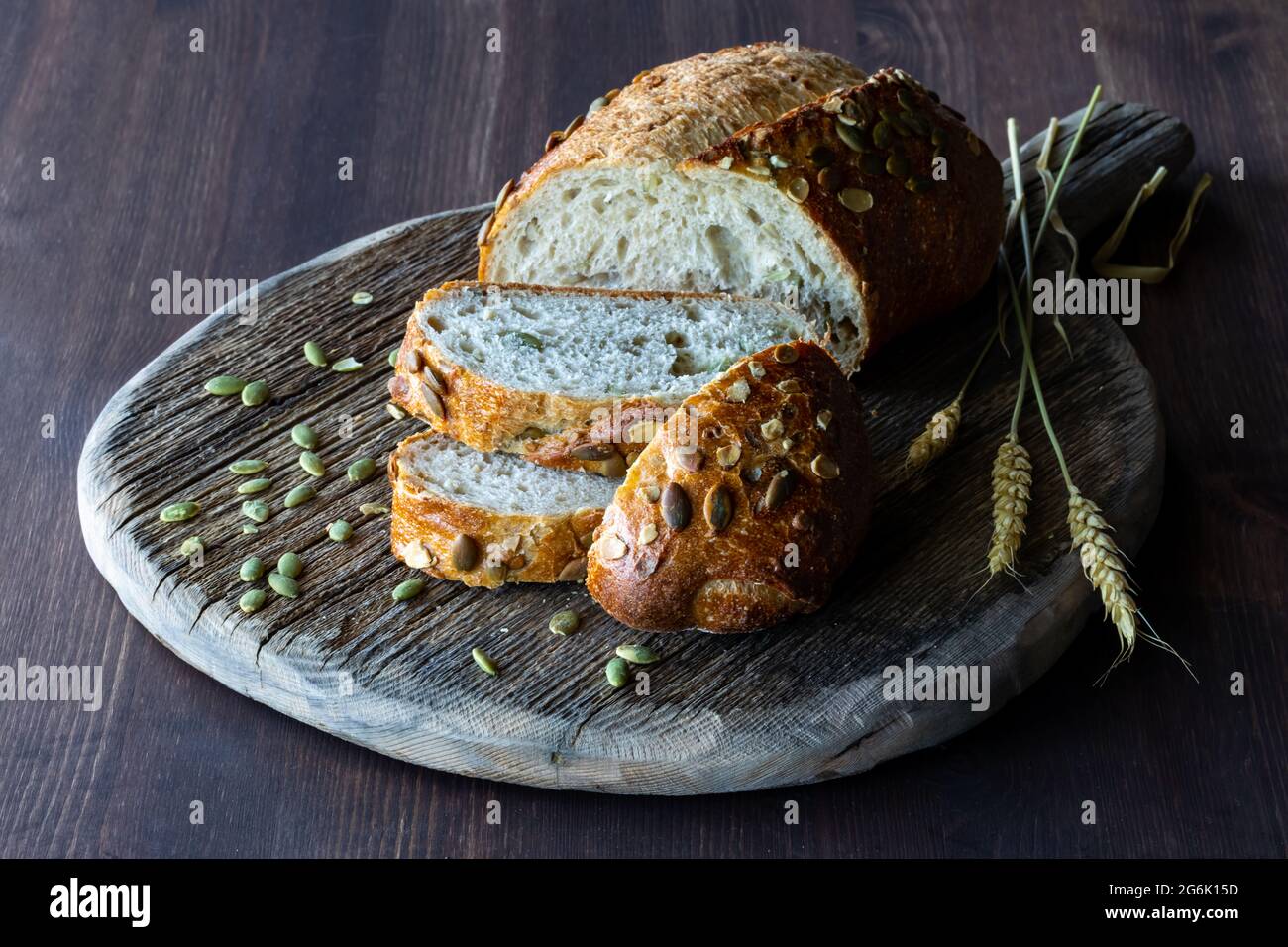 Close up view of a loaf of pumpkin seed bread sliced into on a wooden board, against a dark background. Stock Photo