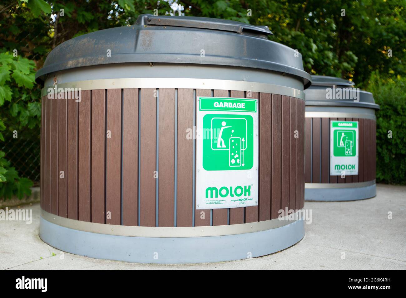 Molok North America Ltd deep waste management  garbage bins are seen under the trees in an outdoor area. Stock Photo