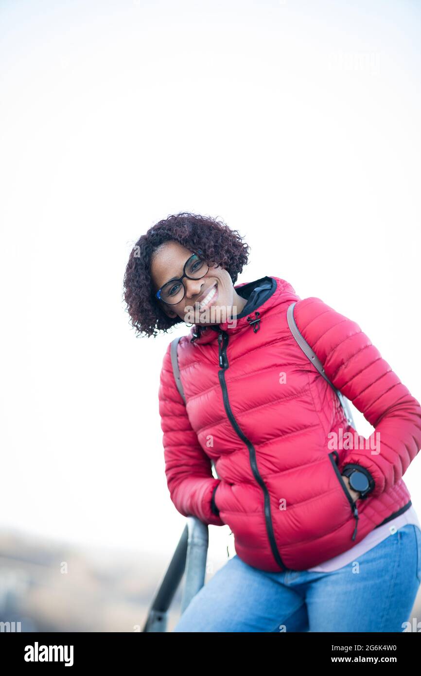 Portrait shot of a joyful African American woman dressed casually in red jacket and jeans, camera focuses on her smiling face Stock Photo
