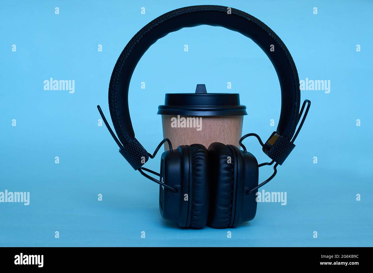 A paper cup for coffee and wireless headphones on a blue background ...