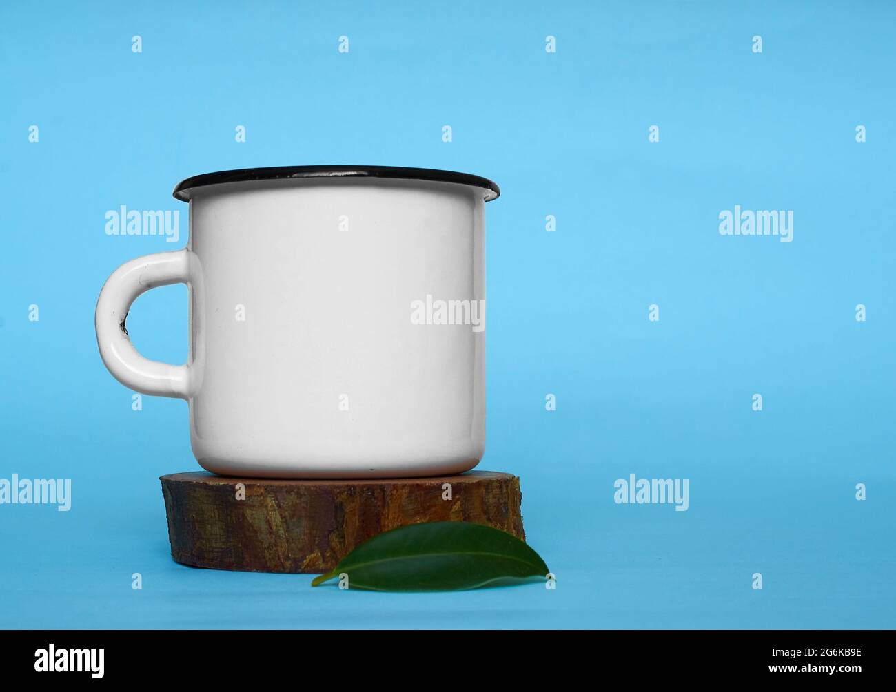 A white metal mug and a green ficus leaf on a wooden stand  Stock Photo