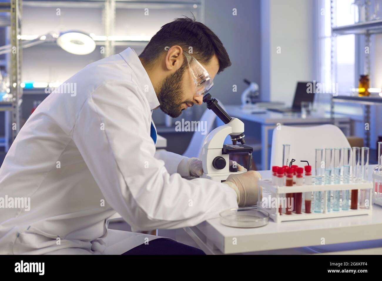 Scientist looking in microscope while doing research in biotech science laboratory Stock Photo