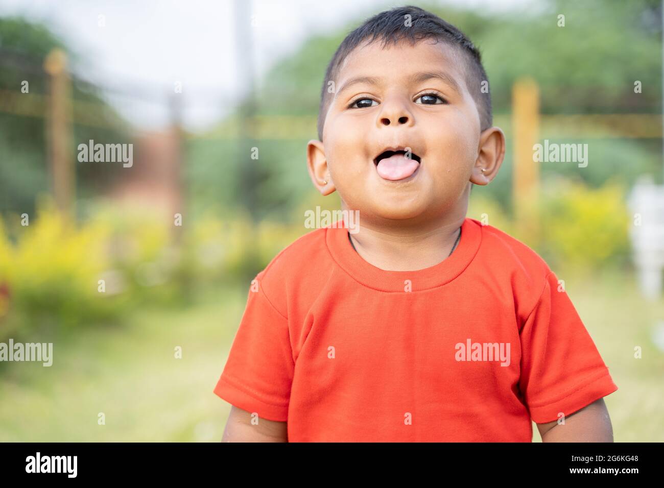 Portrait of Cute little Indian toddler grimacing by making tongue out while playing at park with copy space Stock Photo