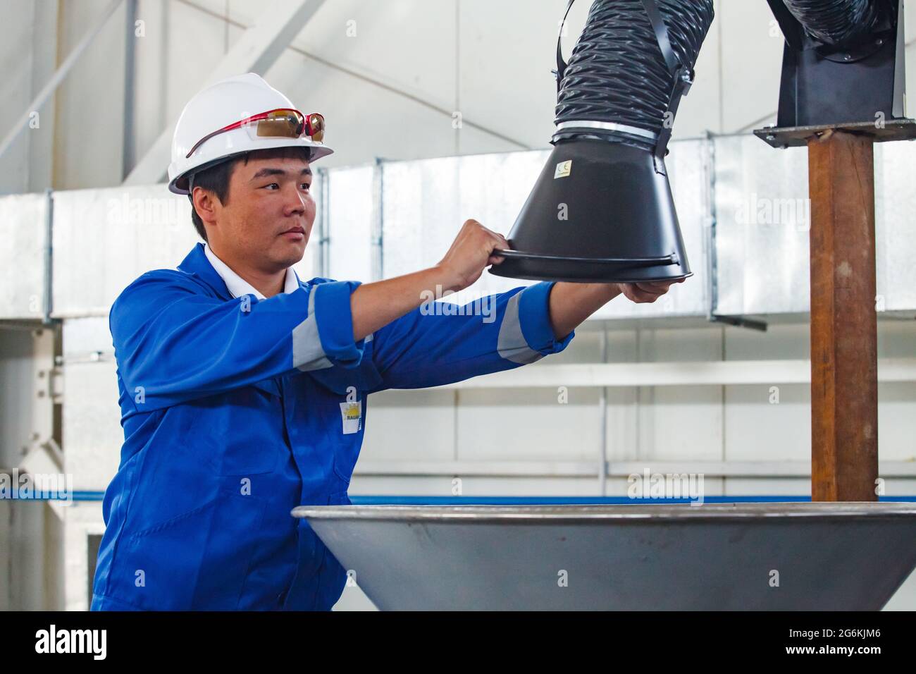 Atyrau,Kazakhstan-May 21,2012: Chemical plant Rauan Nalco. Young Asian worker adjusting fume extractor arm with hood. White hardhat, protective glasse Stock Photo
