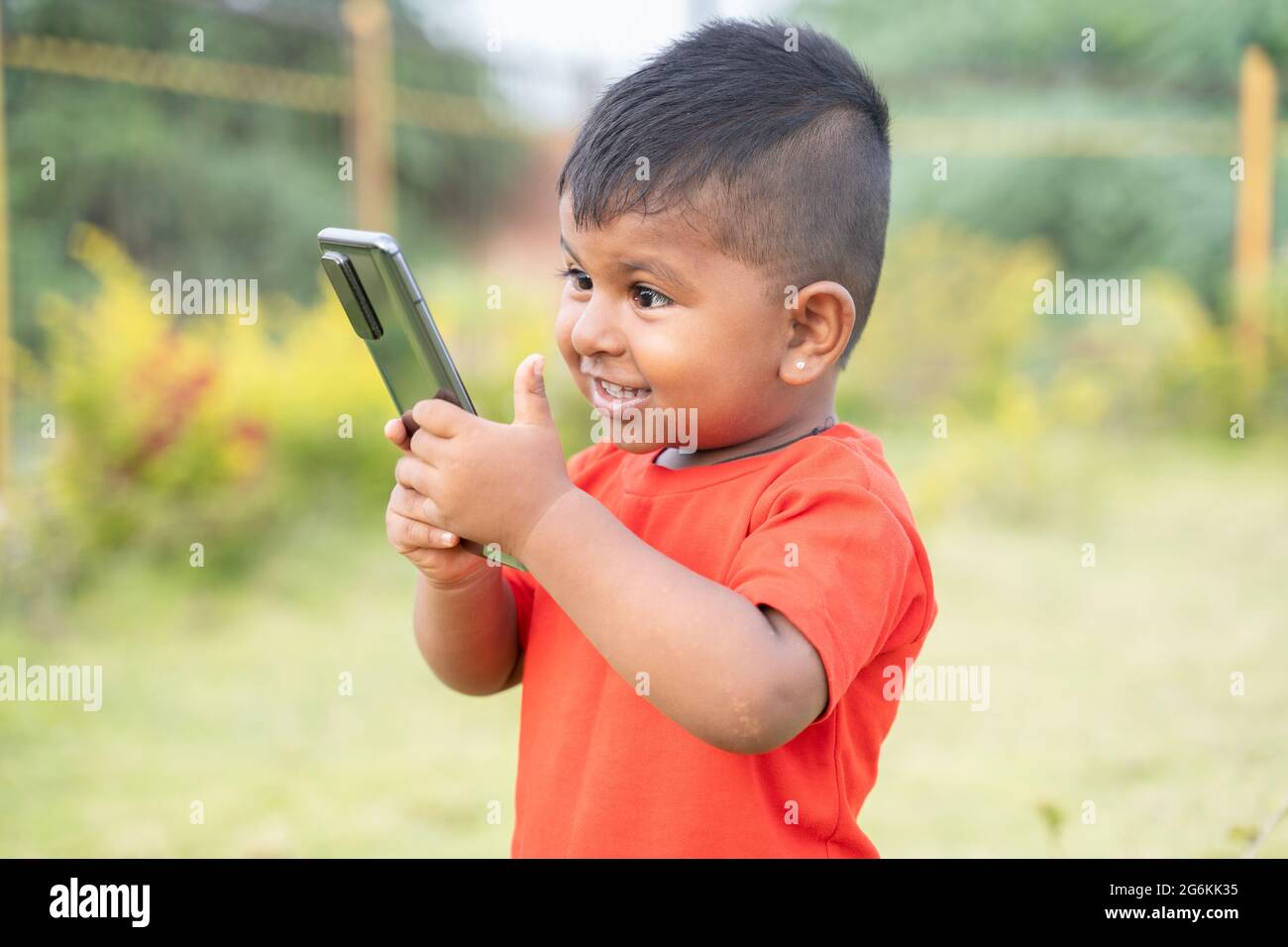 Portrait of Excited surprised Indian chubby kid Laughing by looking into mobile phone - Concept of Children Mobile addiction, internet and technology. Stock Photo