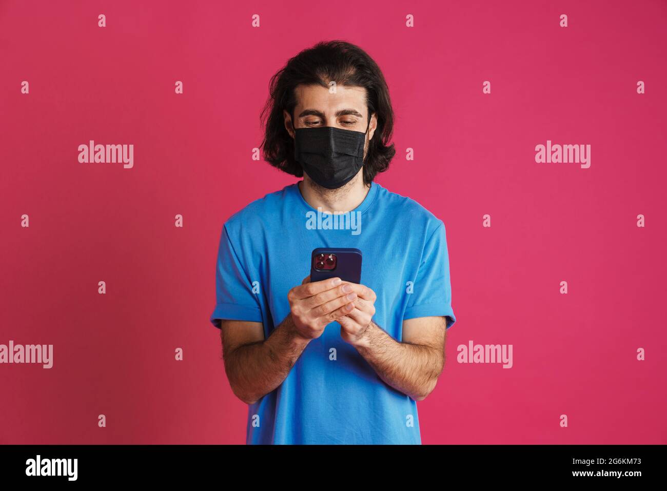 White brunette man in face mask using mobile phone isolated over pink background Stock Photo