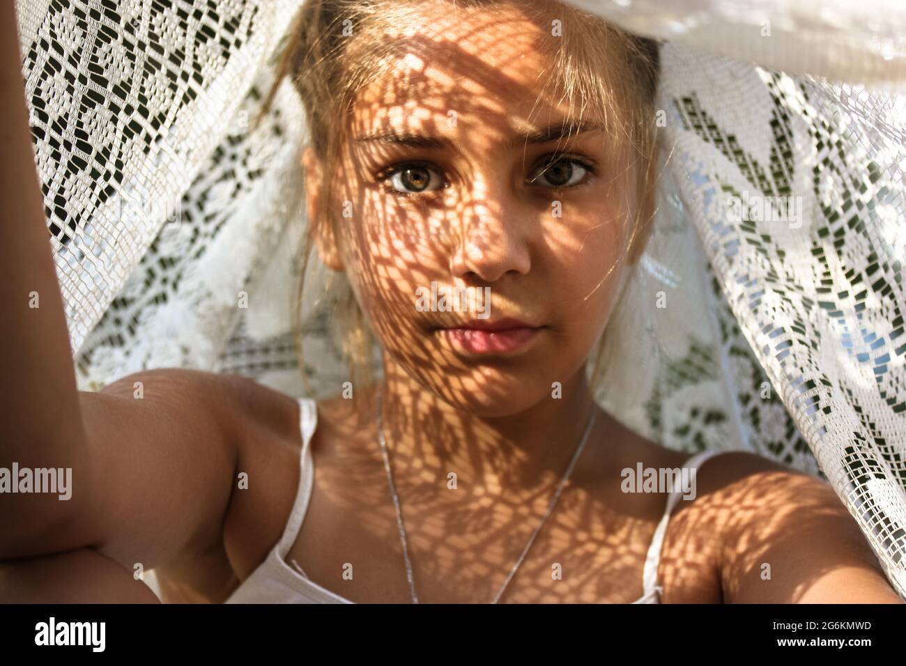 Mysterious portrait of a beautiful mestizo young girl with light shadow pattern on face. Adorable charming green eyed female looking at camera. Creati Stock Photo