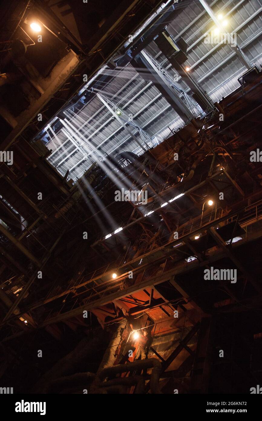 Aksu, Kazakhstan - May 29, 2012: Interior of electric power plant with boiler. Welder down. Sun rays in steamed air. Profile roof. Stock Photo