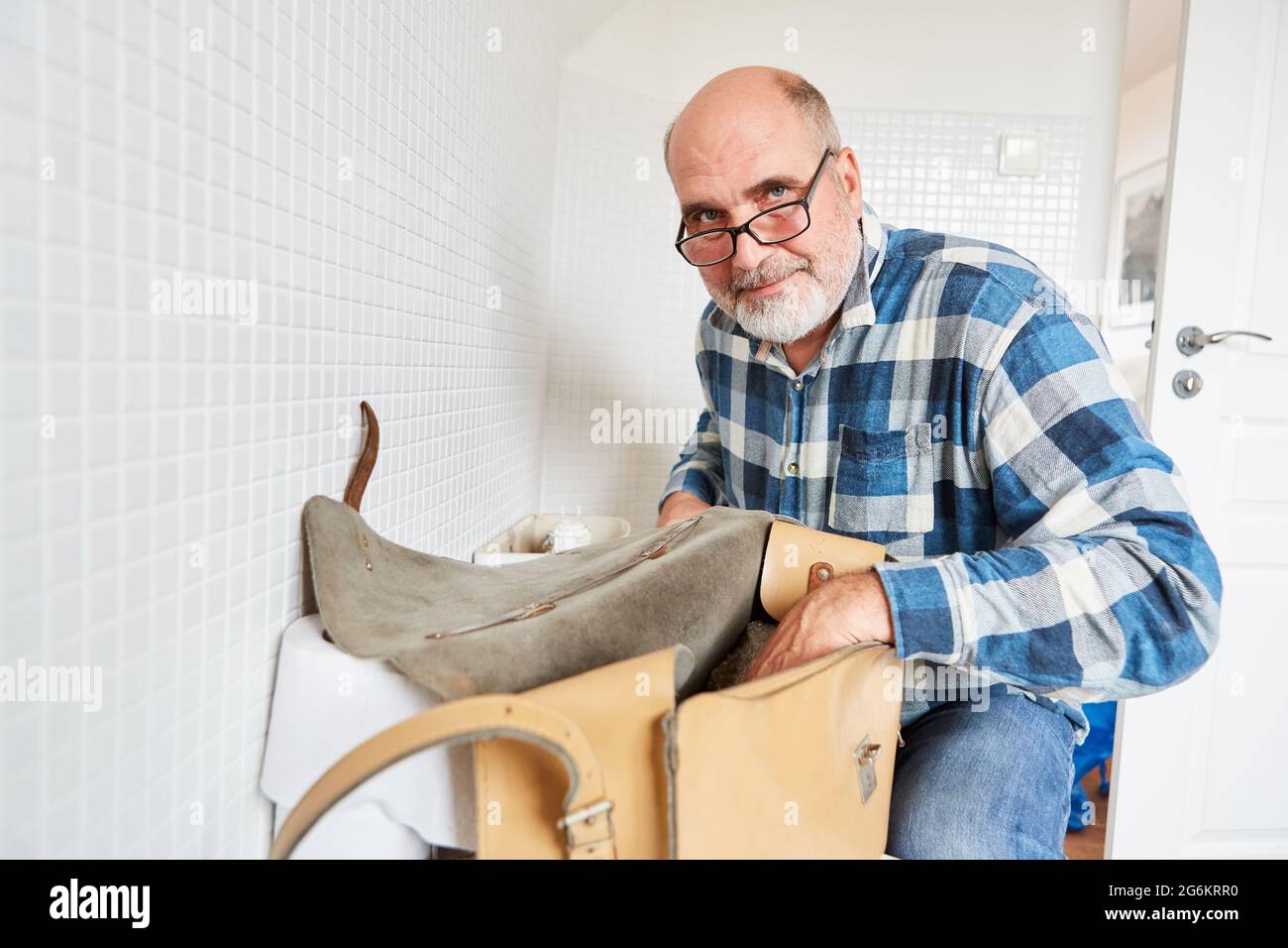 Caretaker as plumber handyman with tool bag repairs broken toilet Stock Photo