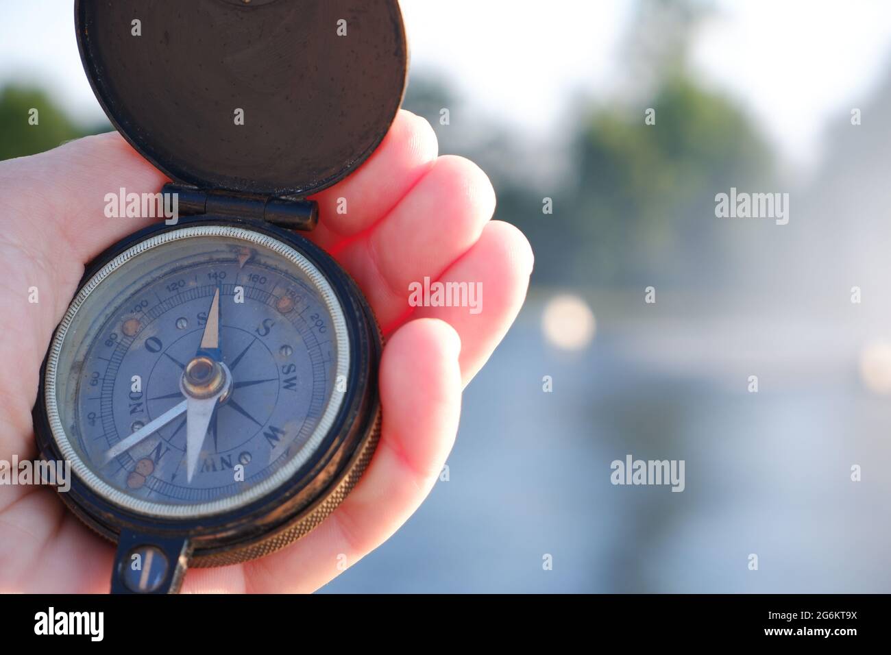 Old compass in the hand of a tourist in front of the reservoir. Stock Photo