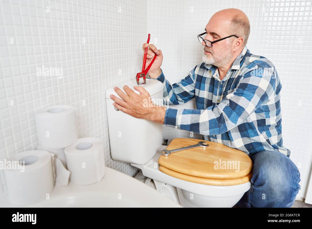 Craftsman or do-it-yourselfer with pipe wrench repairs the cistern in the toilet Stock Photo