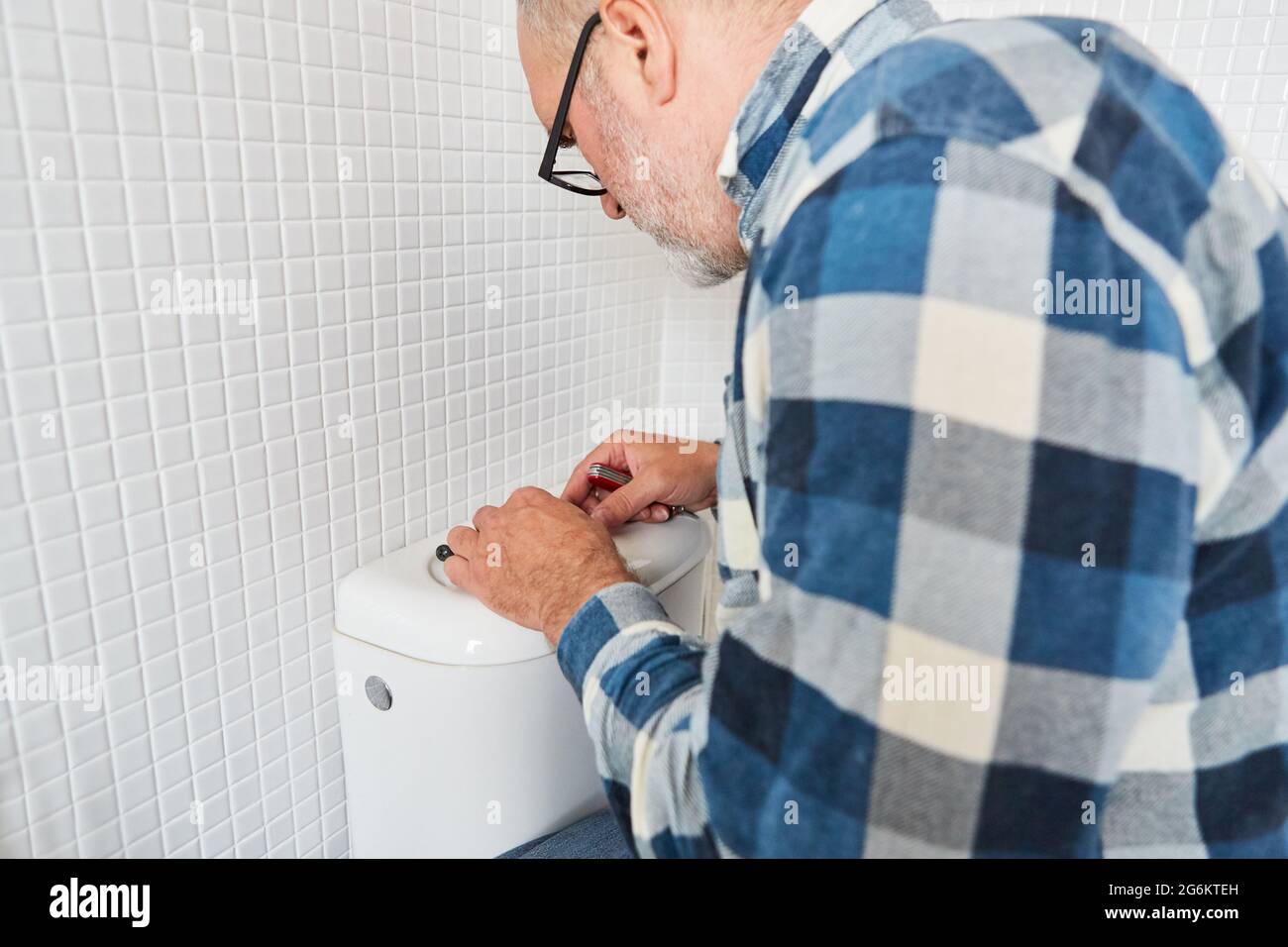 Craftsman plumber repairs defective toilet flush on the cistern in the toilet Stock Photo