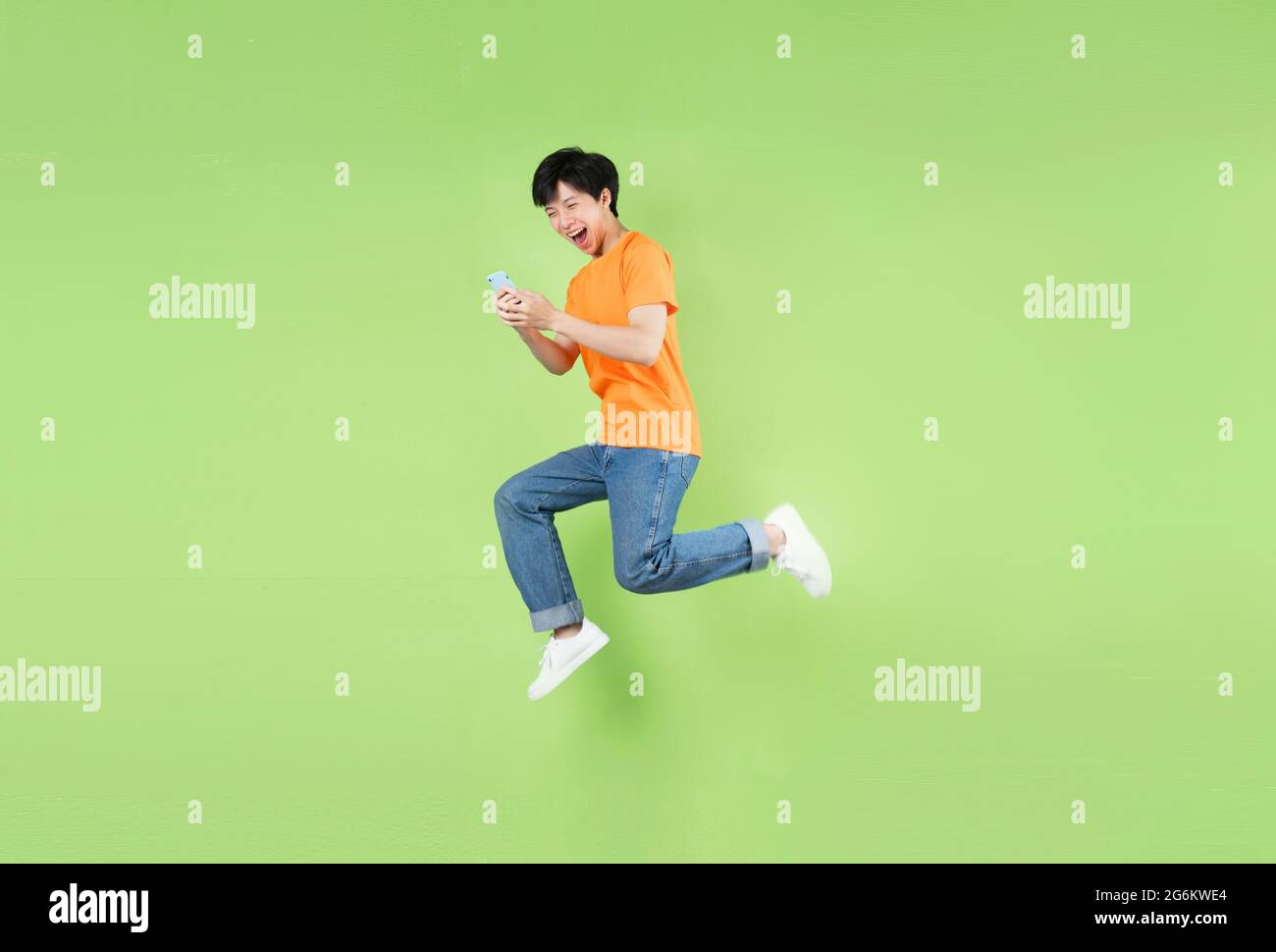 Asian man jumping and holding smartphone , isolated on green Stock Photo