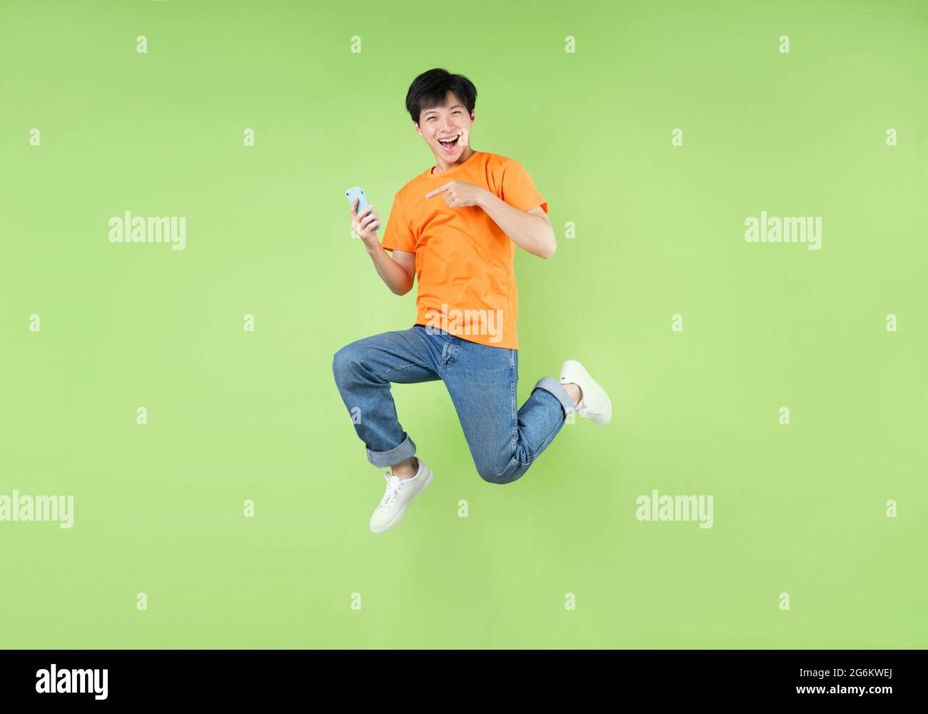 Asian man jumping and holding smartphone , isolated on green Stock Photo
