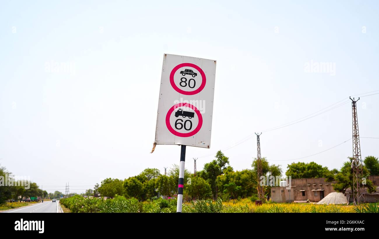 Limit Speed Sign Board of running vehicles with 80 and 60 speed. Vehicles passing through road against blue sky background. Stock Photo