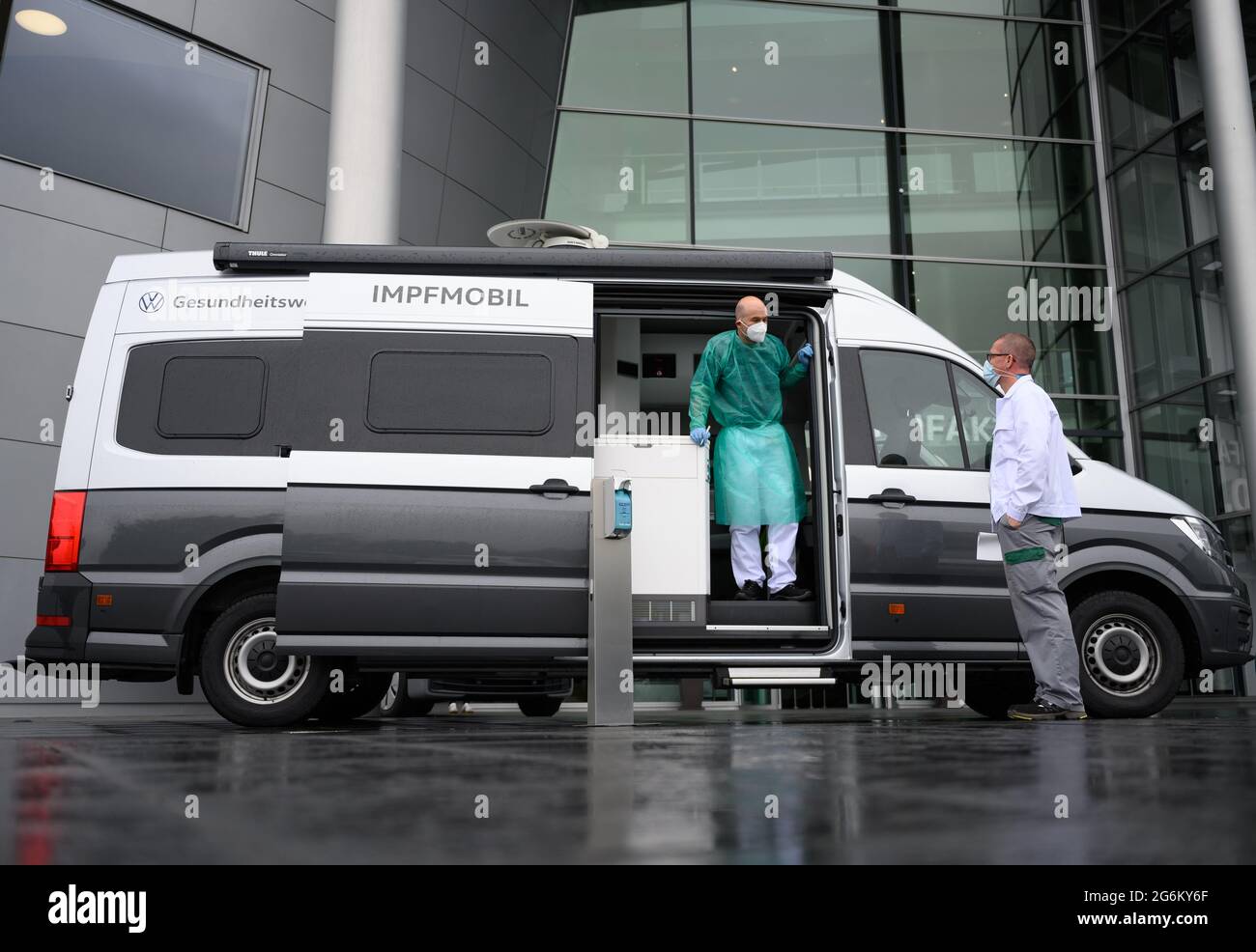 07 July 2021, Saxony, Dresden: Lars Becker (l), company doctor at VW  Saxony, stands in front of the Transparent Factory in a camper van  converted into a vaccination vehicle and welcomes an