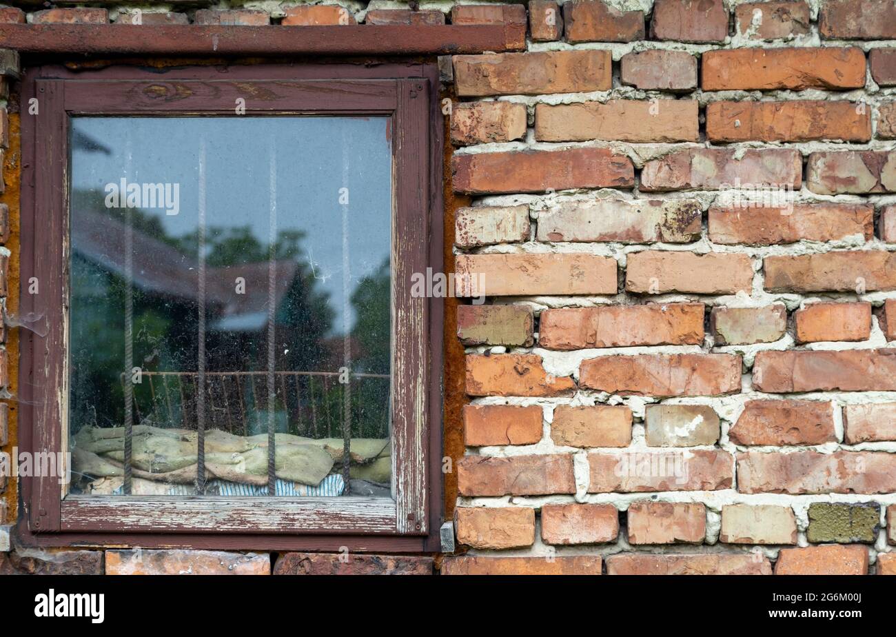 Old brick wall with a wooden window. With metal grilles. Display of an old house in the window Stock Photo