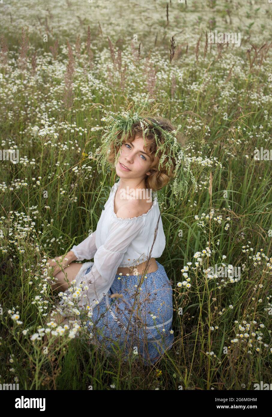 romantic beautiful young woman sits among a field of wild white daisies. digital detox, weekend in nature, search for inspiration, enjoyment of the mo Stock Photo