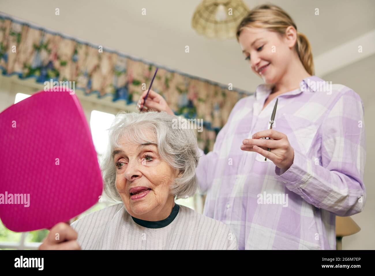 Female Mobile Hairdresser Cutting Senior Womans Hair At Home Stock Photo