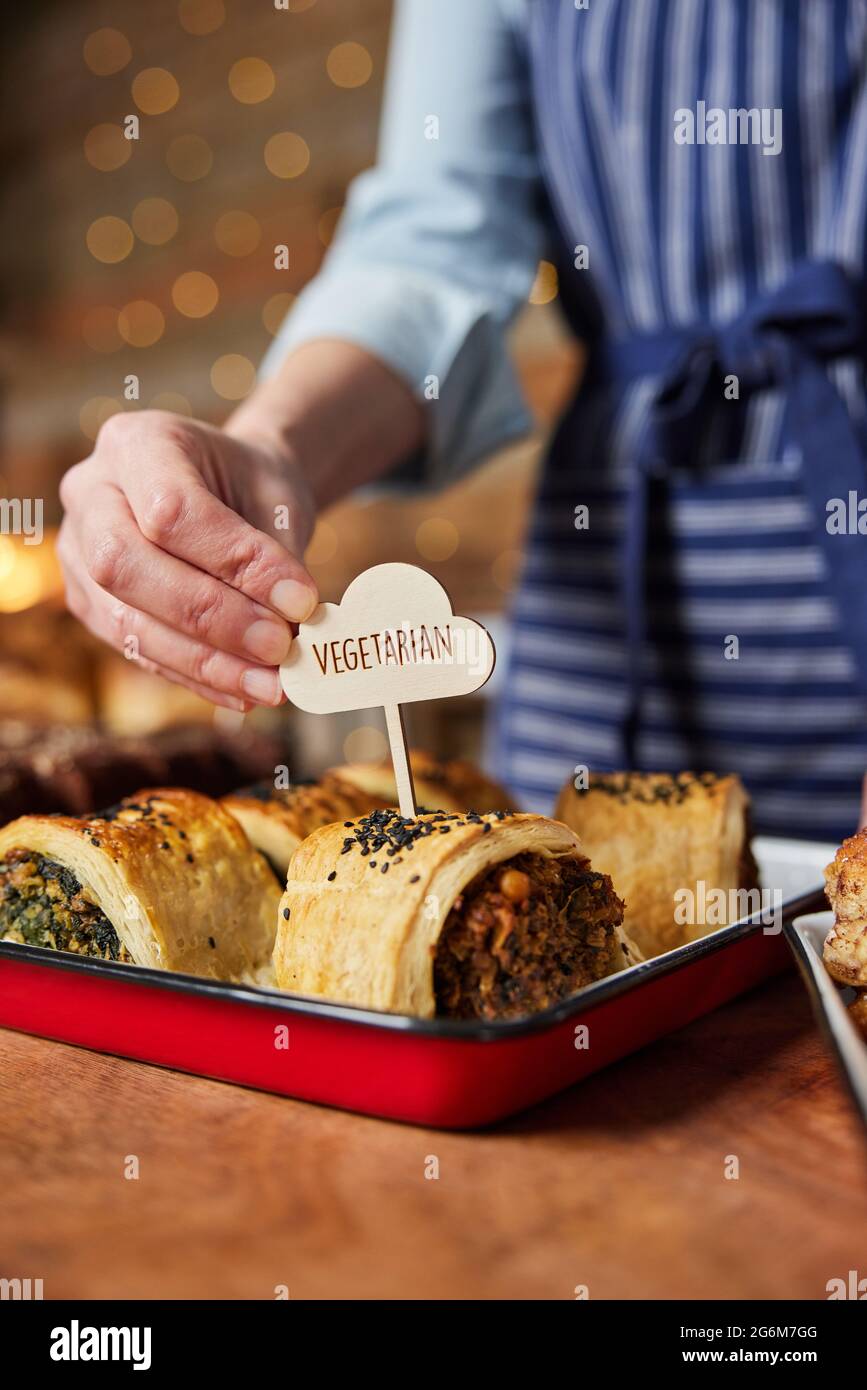 Sales Assistant In Bakery Putting Vegetarian Free Label Into Freshly Baked Savoury Roll Stock Photo