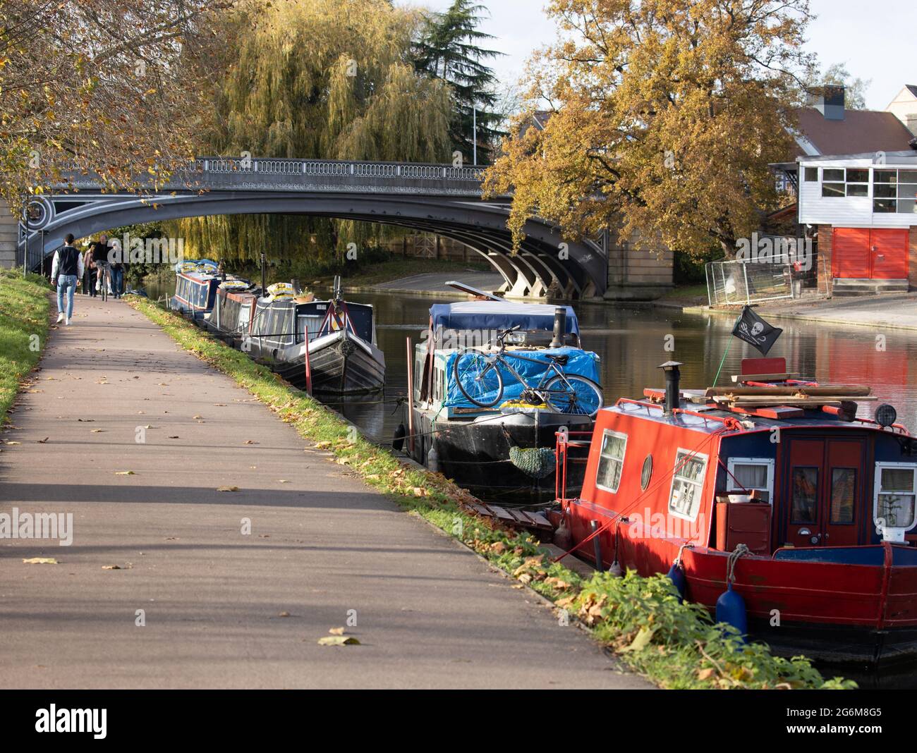 Pretty scene of the River Cam in Cambridge with colourful boats moored along the river bank with people walking along riverside path Stock Photo